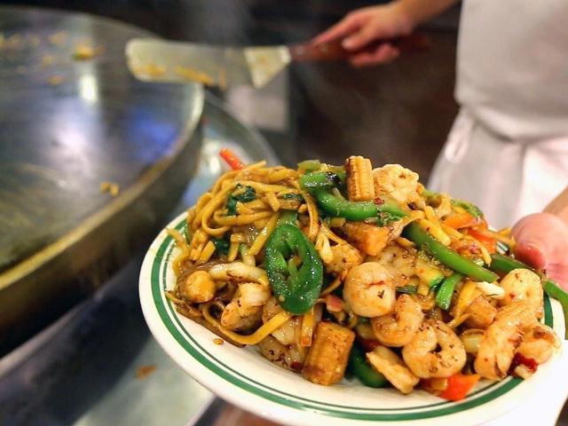 A chef holding a plate of noodles with shrimp and peppers fresh off the grill